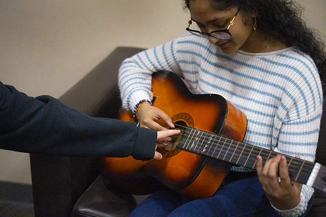 person playing guitar with someone teaching